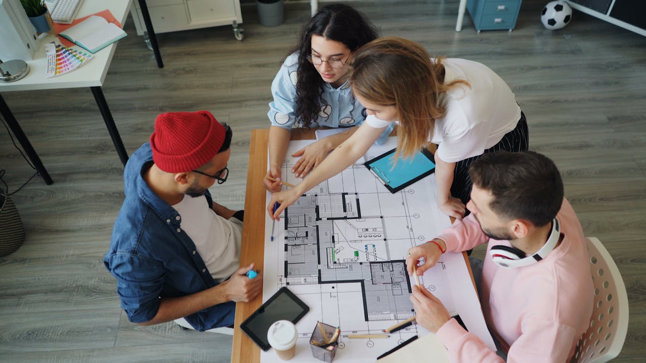 who-we-are-img Young creative professionals discussing an architectural blueprint in a modern office setting.