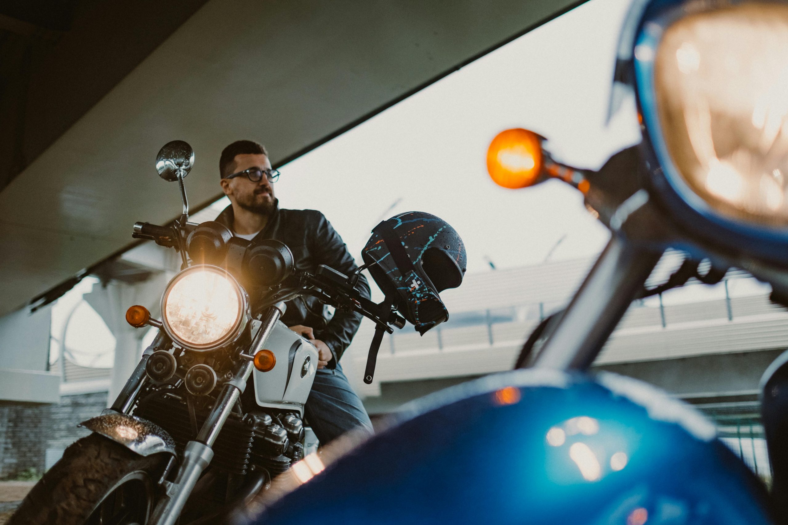 A man on a vintage motorcycle sitting under an urban bridge, exuding a cool and adventurous vibe.