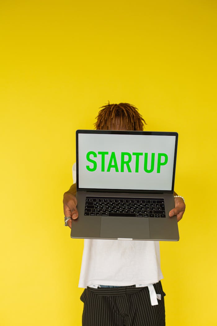 services-01 Person holding a laptop with 'STARTUP' text against a bright yellow background, symbolizing innovation.